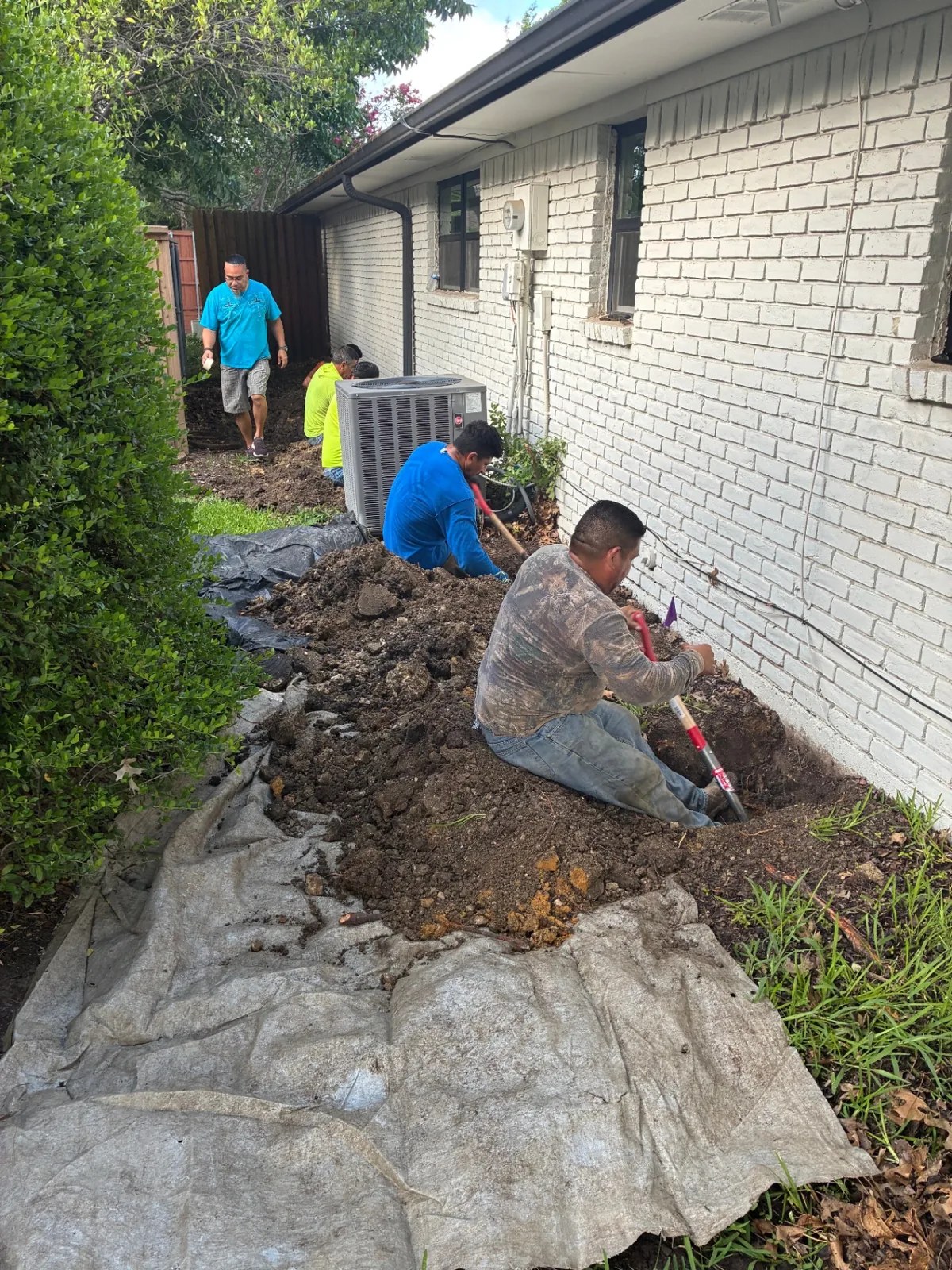 Crew excavating along the exterior brick wall of a home during foundation repair